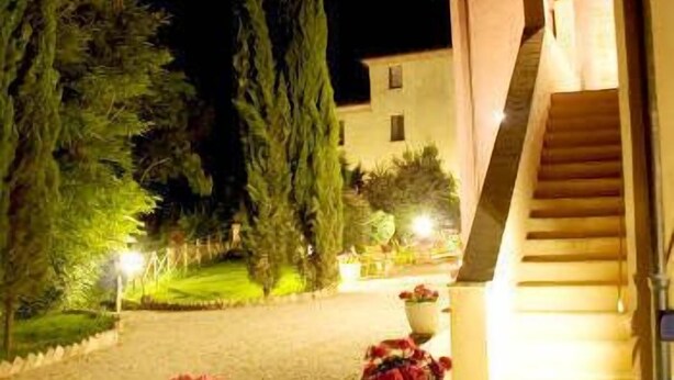 A nighttime view of a building with a staircase leading to a door, surrounded by greenery and a well-lit pathway. - Borgo Dolciano (Chiusi)