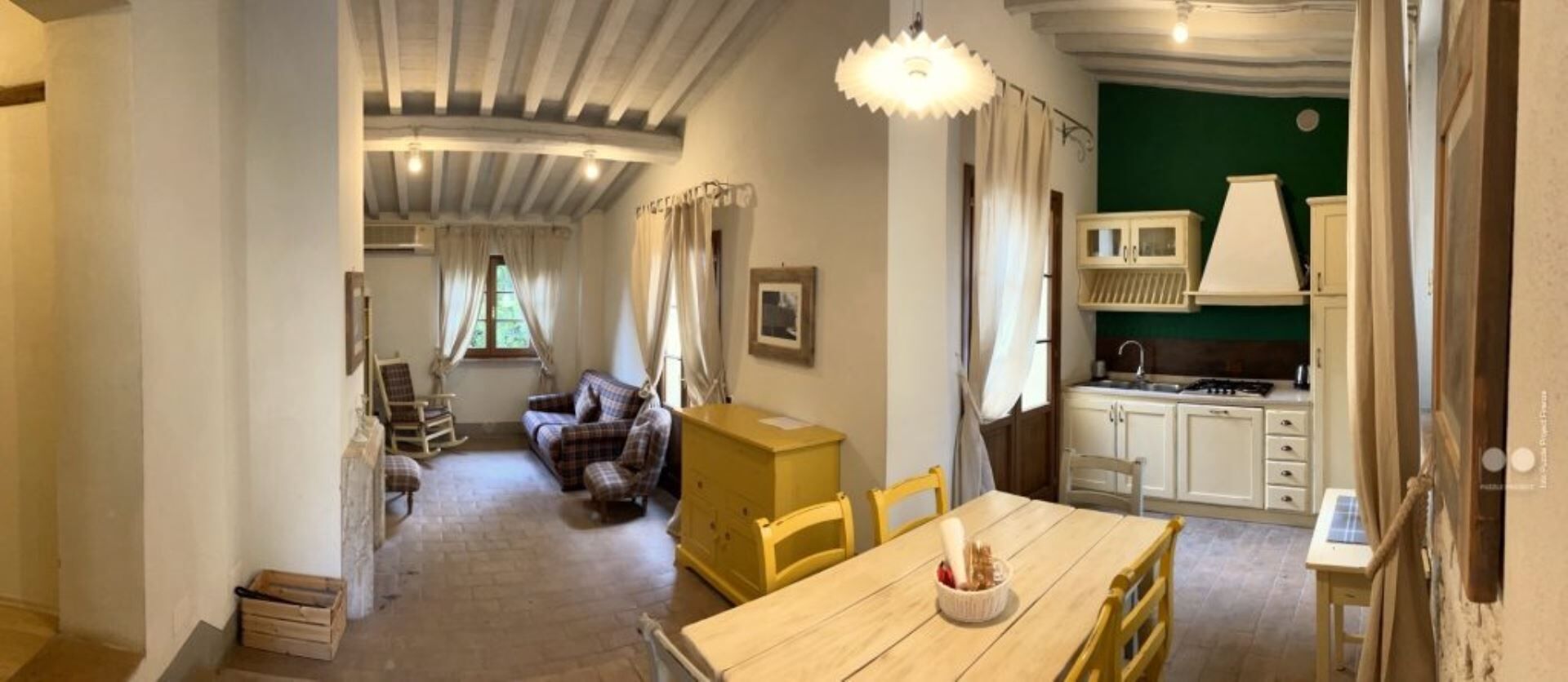 A cozy room with a wooden dining table, a sofa, and a kitchen area with white cabinets and a green wall.