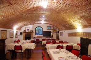A dining hall with brick vaulted ceilings, multiple tables set for dining, and red chairs. - Borgo Dolciano (Chiusi)