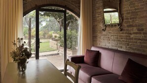 A room with a stone wall, a cushioned bench, and a table with a vase of flowers. - Borgo Dolciano (Chiusi)