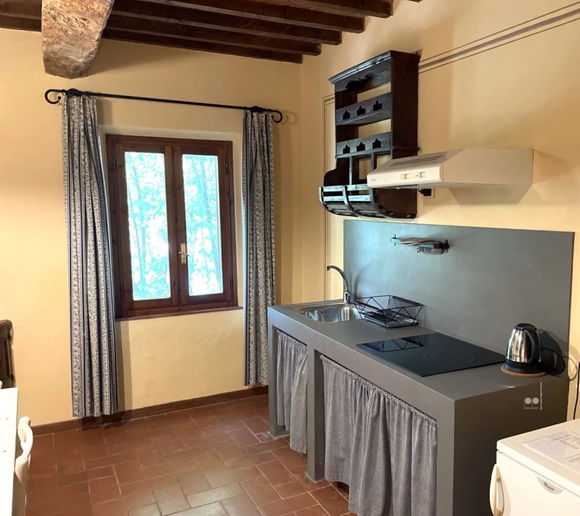 A compact kitchen with a built-in stove, a sink, and a window with curtains.