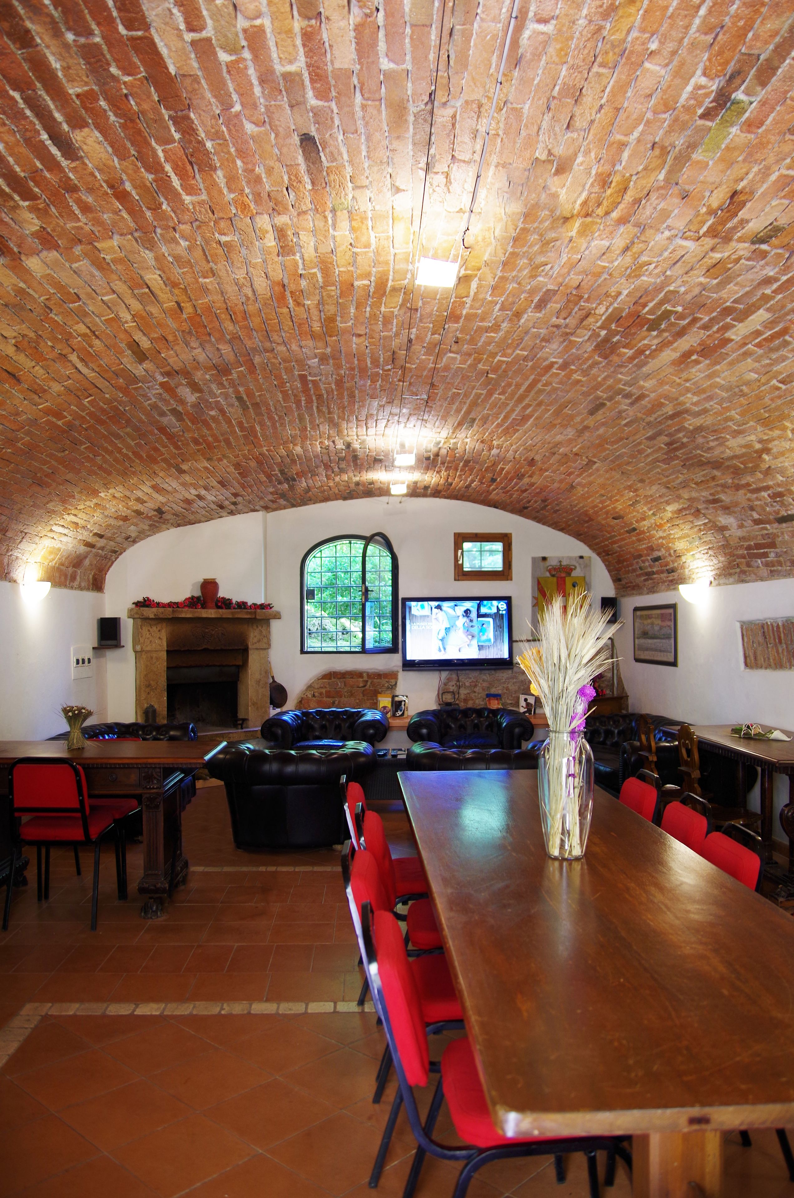 A spacious room with a high arched brick ceiling, a fireplace, a television, and comfortable seating.