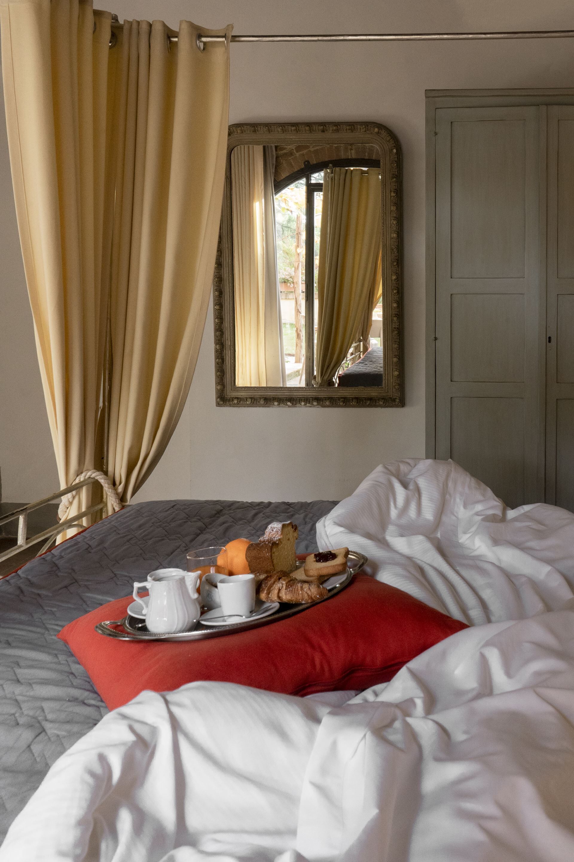 Ein ordentlich bezogenes Bett mit einem Frühstücksbrett, einem Spiegel und einer Tür in einem Hotelzimmer.