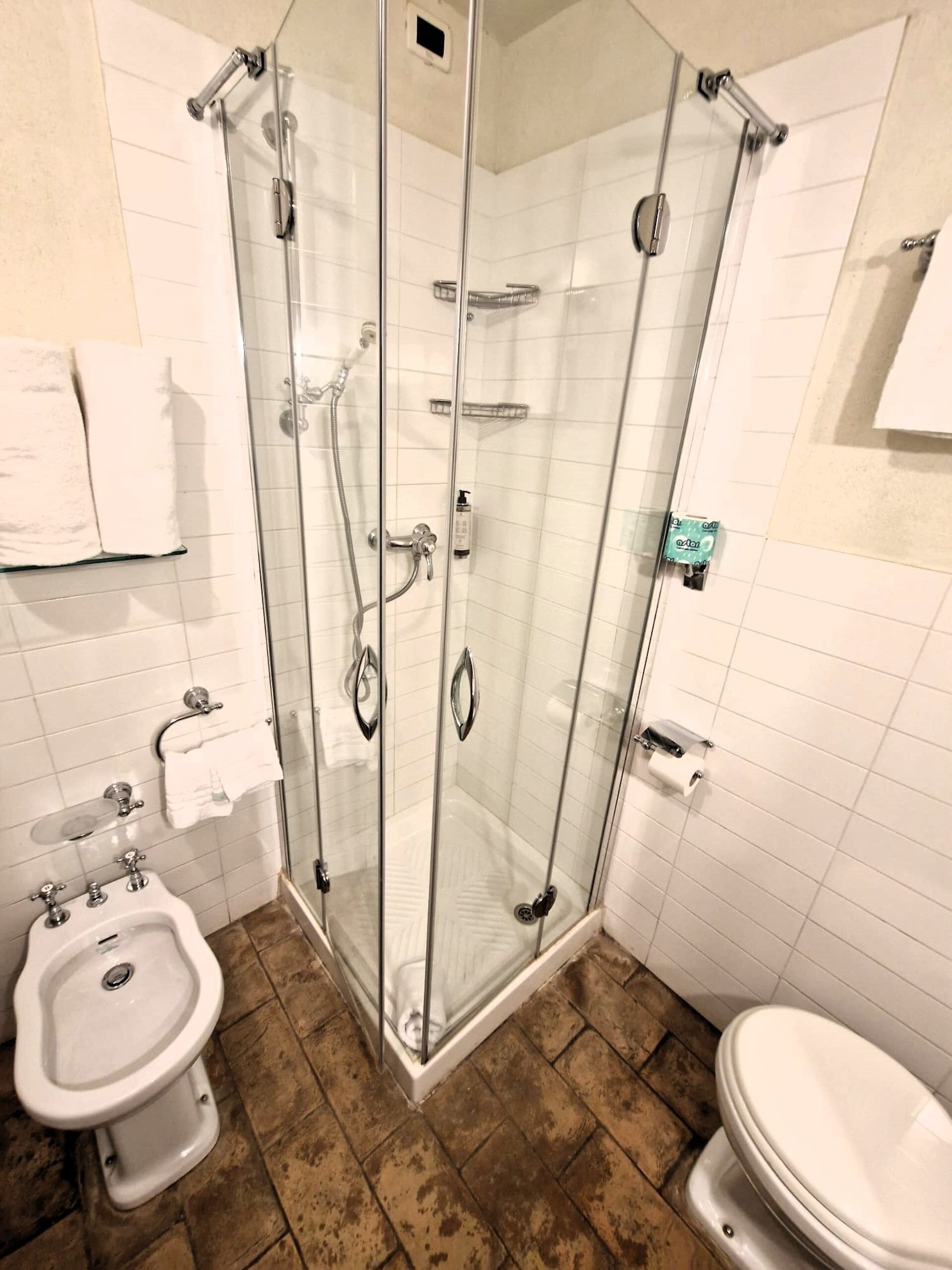 A bathroom with a glass-enclosed shower, a bidet, a toilet, and a sink.