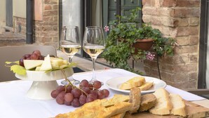 An outdoor table with a white cloth, a bowl of grapes, two glasses of white wine, and a plate of bread. - Borgo Dolciano (Chiusi)