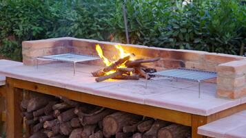 An outdoor grill with two grilling stations, surrounded by a brick wall and a stack of firewood.