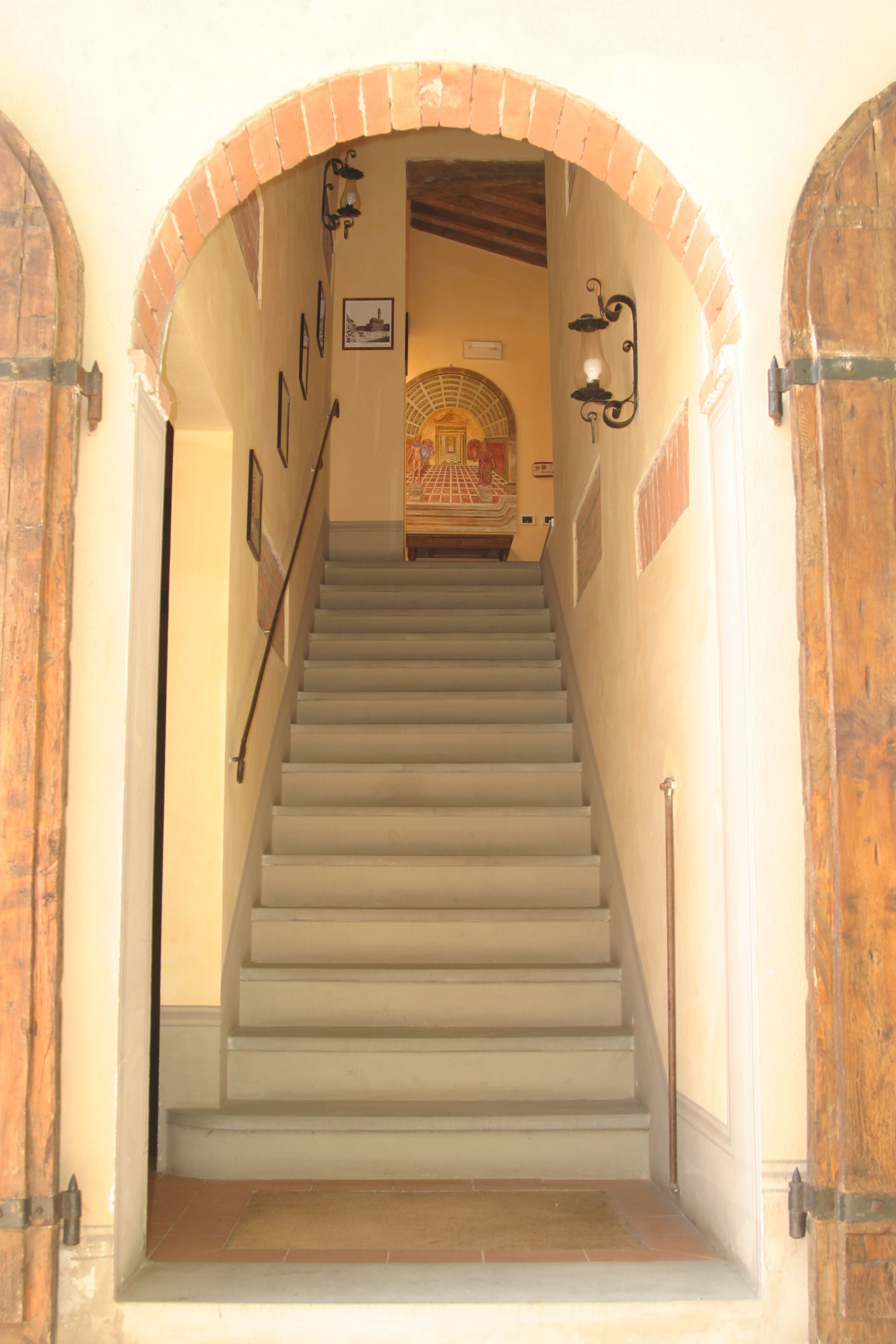 Una escalera con un arco de ladrillo que conduce a una habitación con piso de baldosas y alfombra estampada.