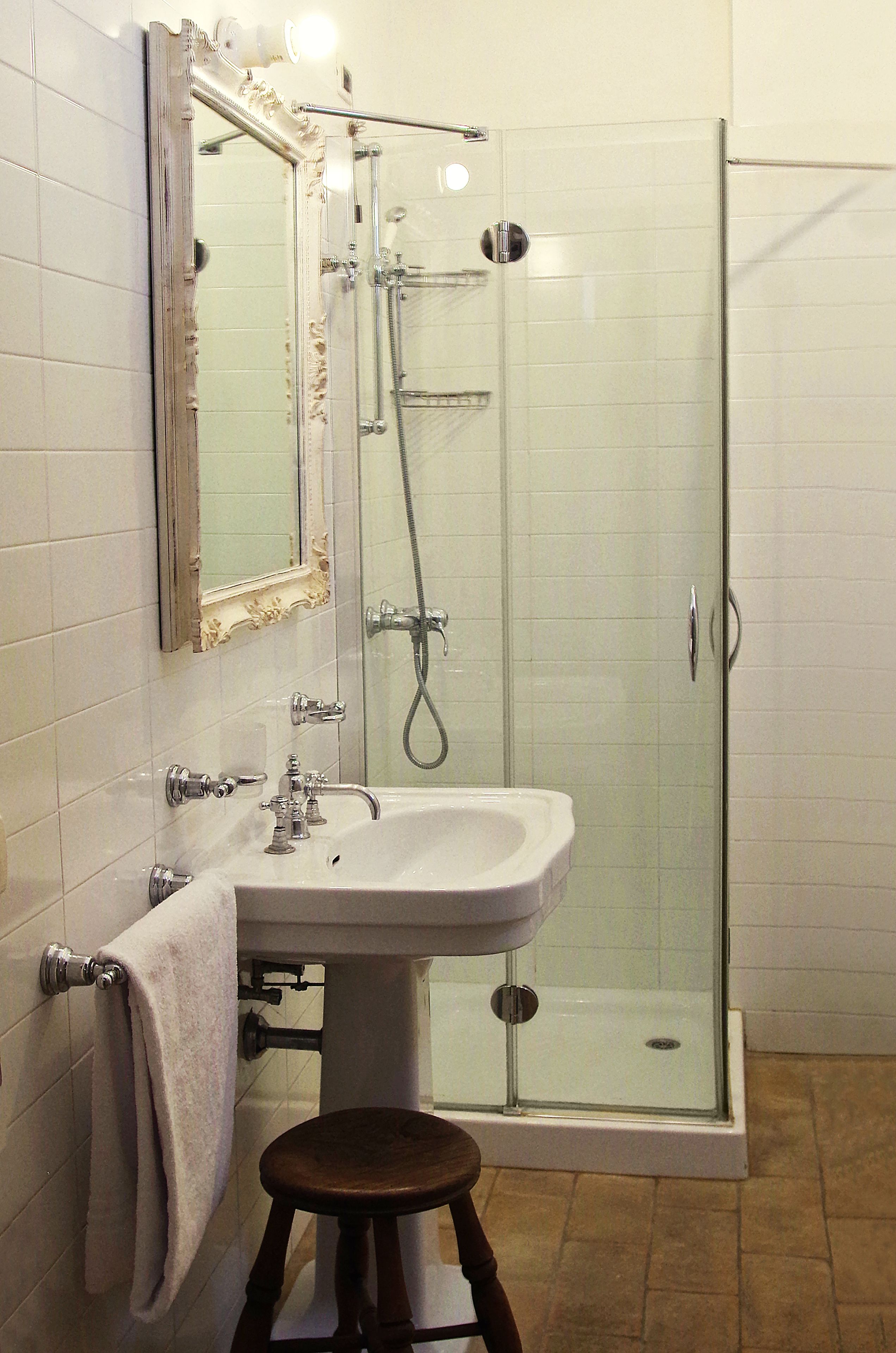 A bathroom with a glass shower enclosure, a pedestal sink, and a mirror with an ornate frame.