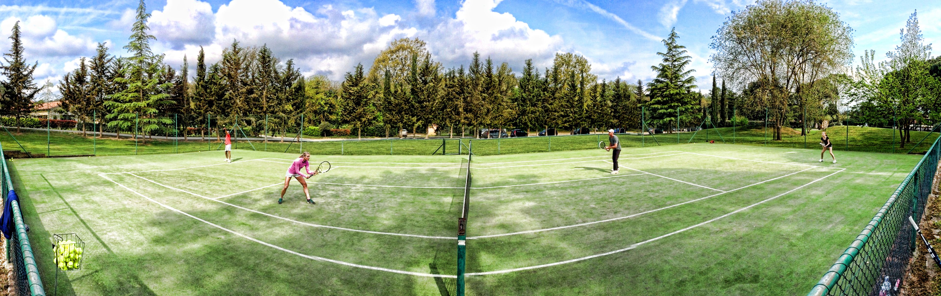 A tennis court with a net, surrounded by trees and a clear sky.