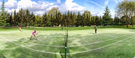 A tennis court with a net, surrounded by trees and a clear sky.