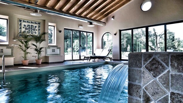 Une piscine agrémentée d’une cascade, de grandes fenêtres et d’un fauteuil de relaxation.