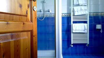 A bathroom with blue tiles, a wooden door, a shower, and a towel rack.