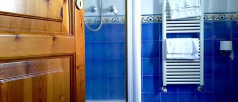A bathroom with blue tiles, a wooden door, a shower, and a towel rack.