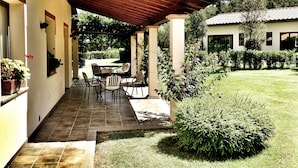 Une terrasse couverte avec une table et des chaises, un petit jardin et un bâtiment en arrière-plan.