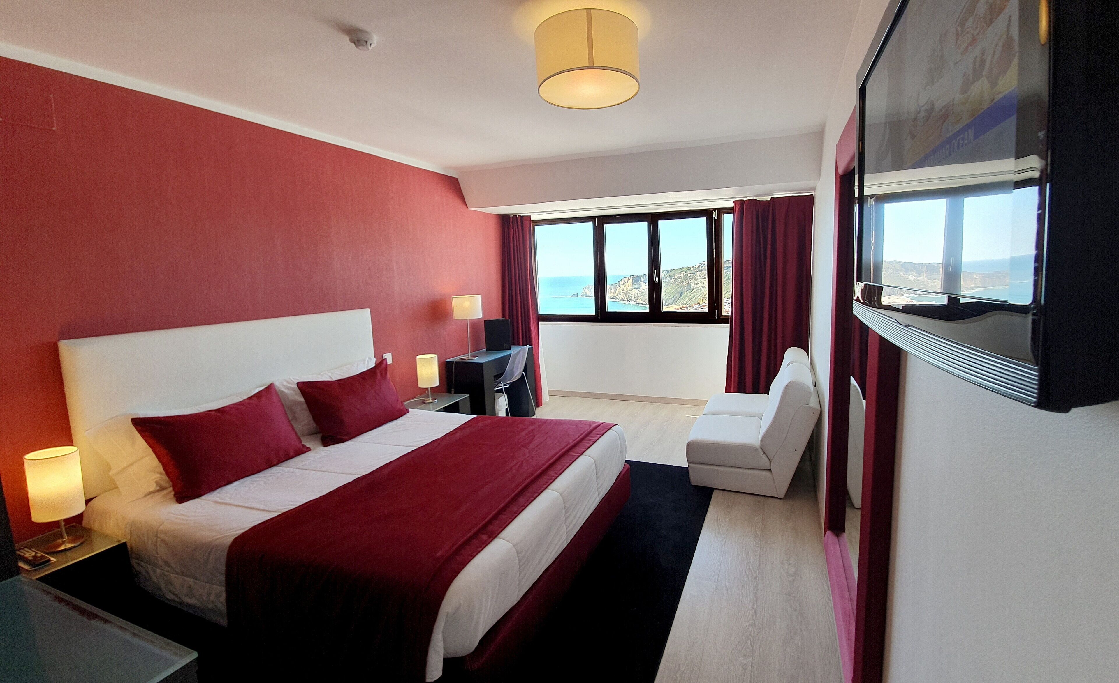 Habitación de hotel con una cama grande, un escritorio, una silla, un televisor y vista al océano.