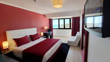 Habitación de hotel con una cama grande, un escritorio, una silla, un televisor y vista al océano.