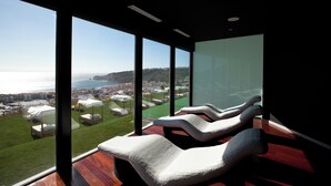 Quarto moderno com amplas janelas com vista para uma paisagem urbana costeira.