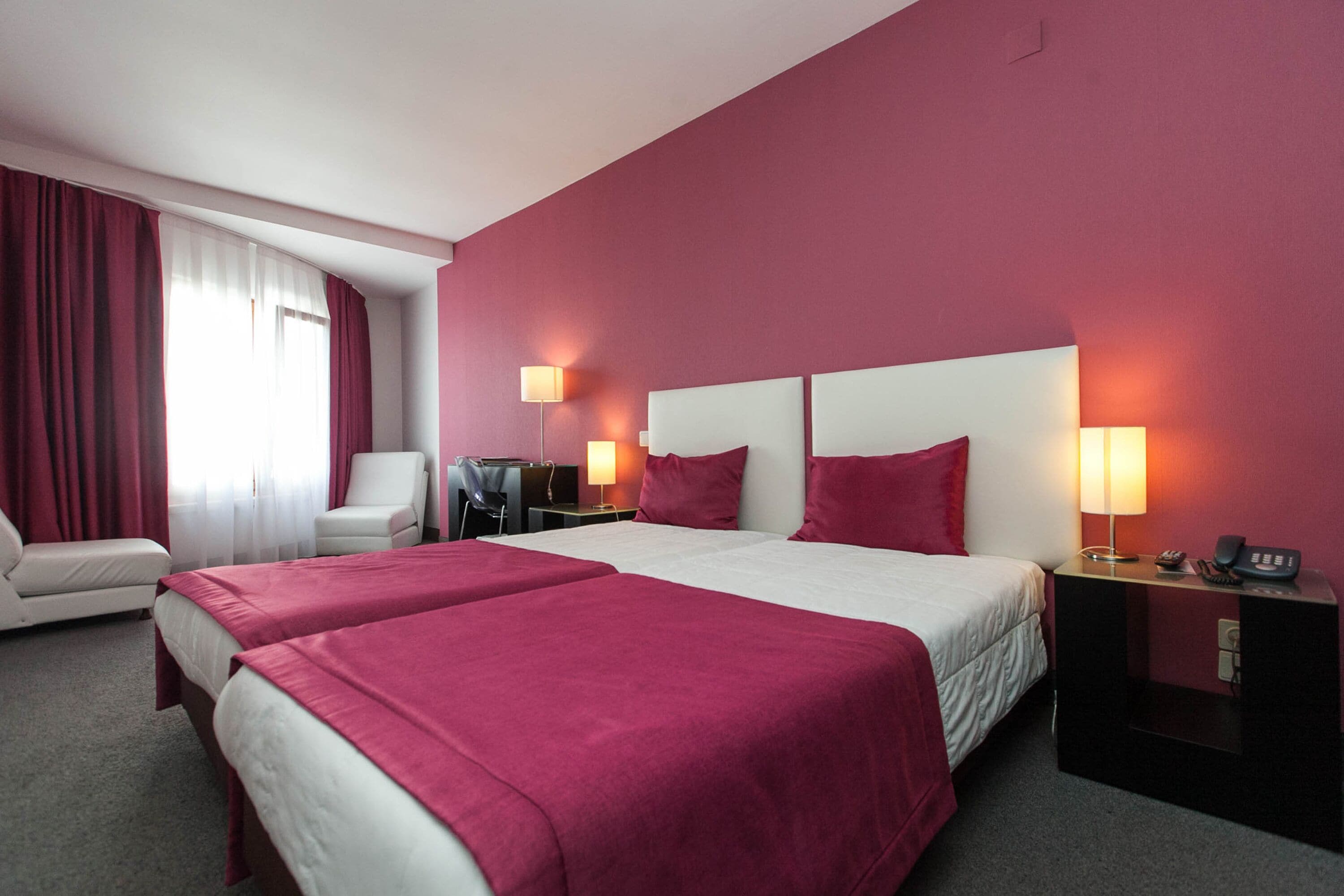 A hotel room with two beds, a desk, a chair, and two bedside lamps.