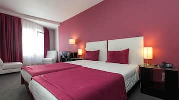 A hotel room with two beds, a desk, a chair, and two bedside lamps.