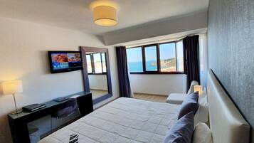 Habitación de hotel con cama, escritorio, televisor, ventana y vista al mar, además de una lámpara.