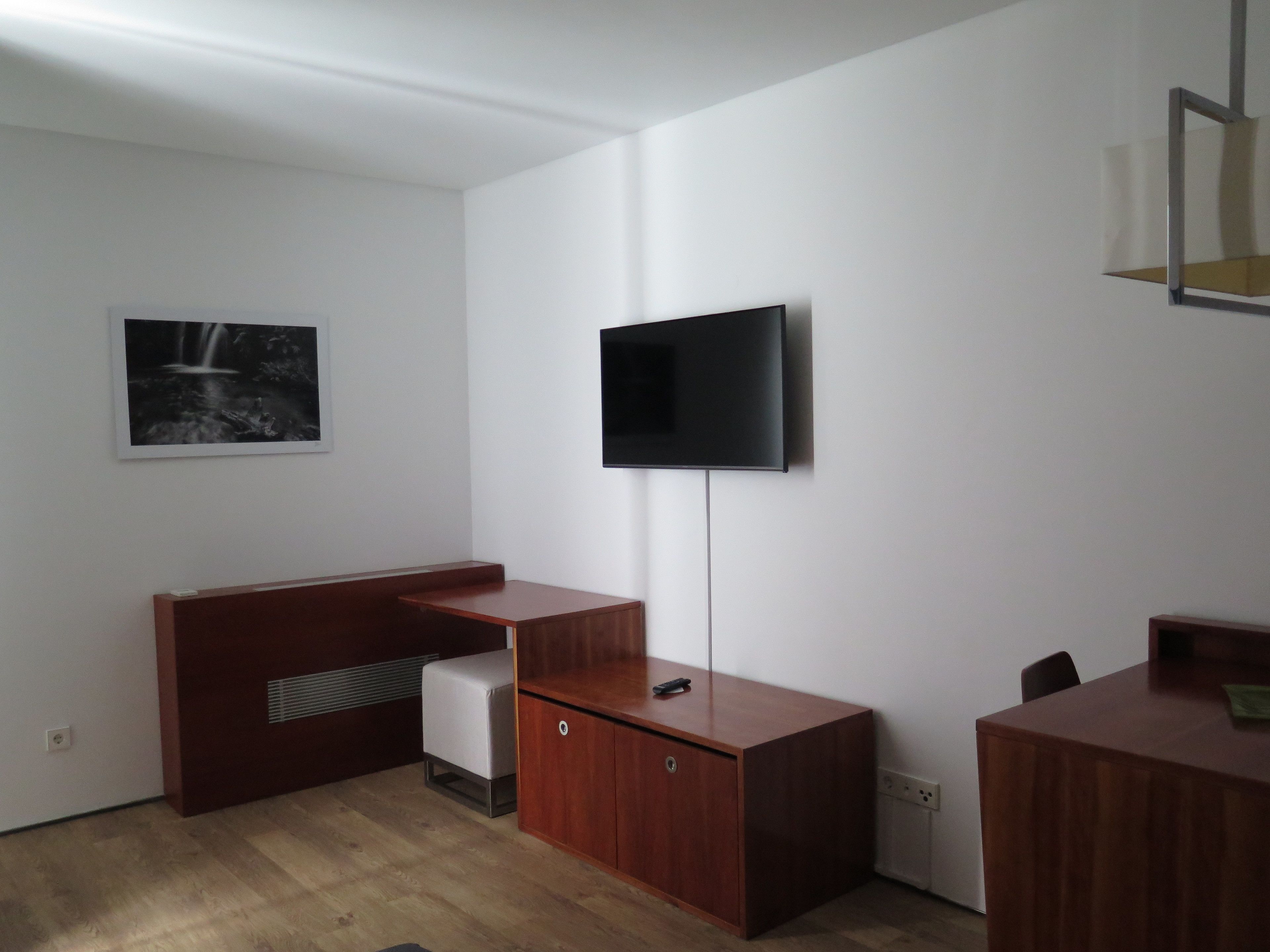 Una habitación moderna con televisor de pantalla plana en la pared, un escritorio de madera y un pequeño sofá.