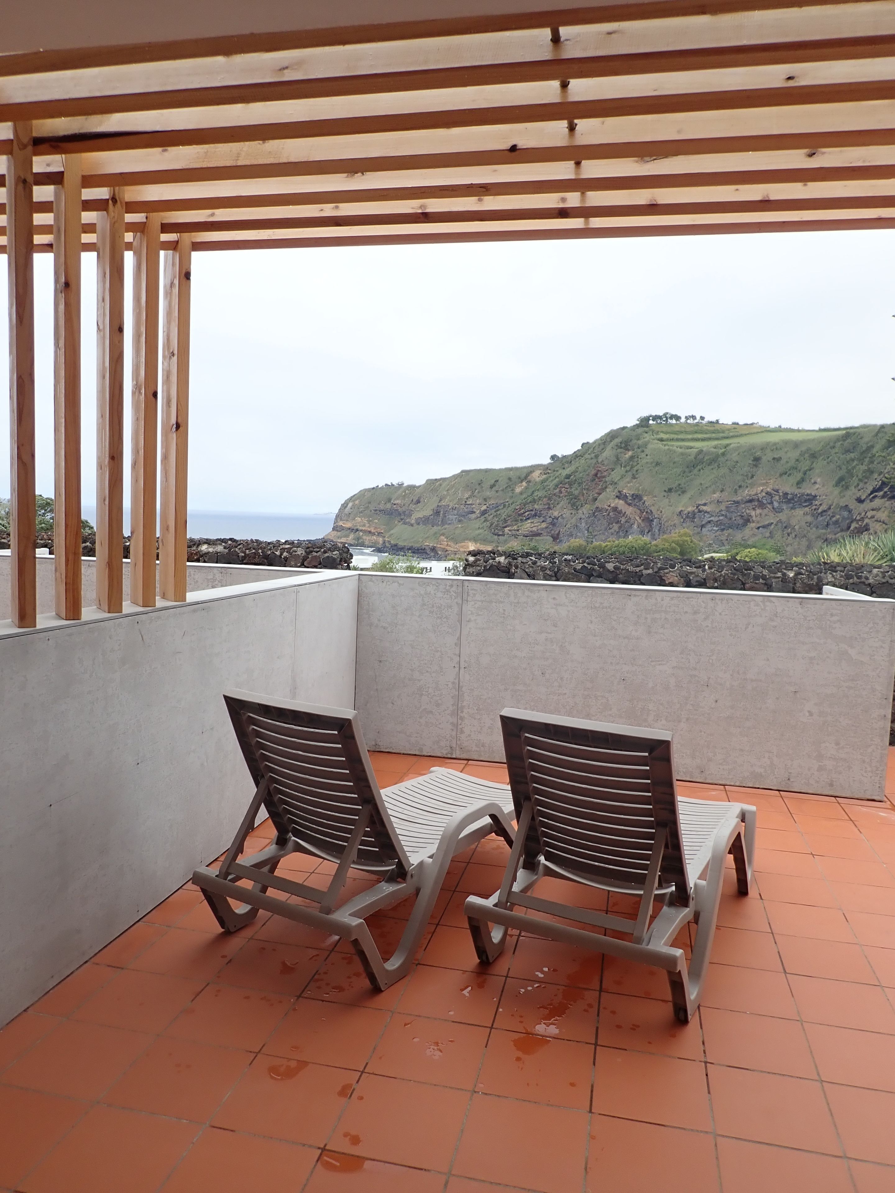 En balkon med to stole og et bord, der ud til et kystlandskab med en klippe og havudsigt i det fjerne.