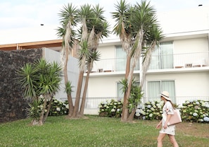 A building with a stone wall, palm trees, and a balcony with flowers.
