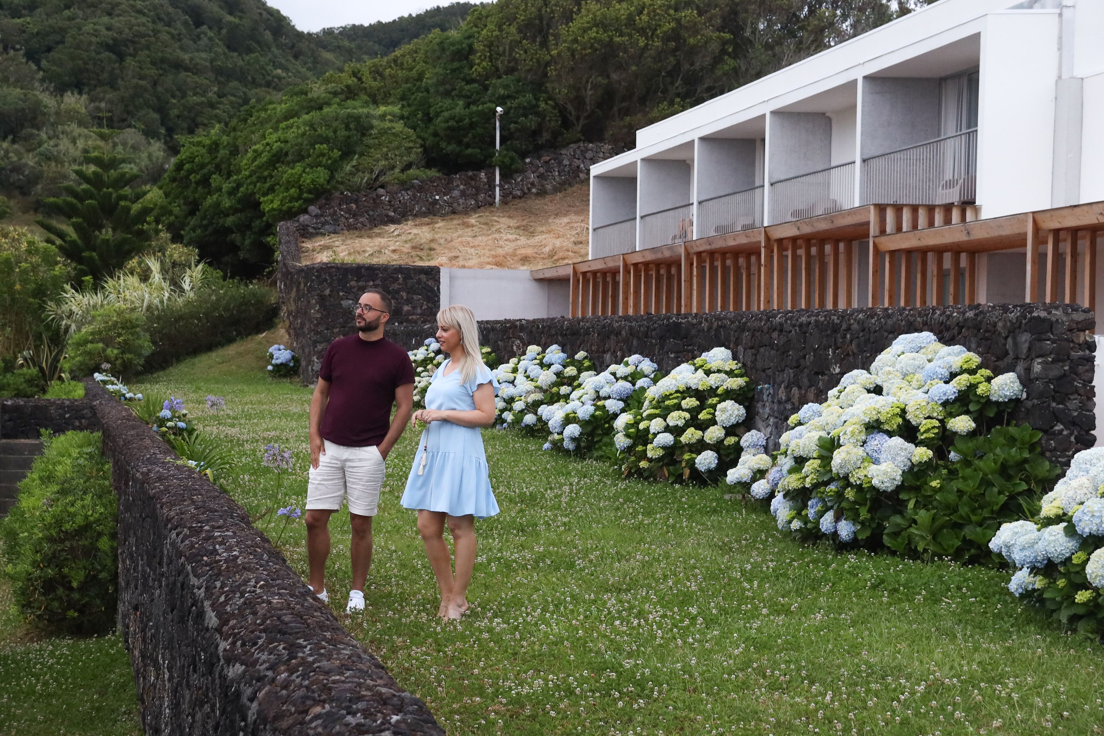 Ein Paar steht in einem Garten mit weißen Hortensien und einer Steinmauer.