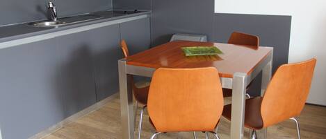 Una cocina moderna con armarios grises, un lavamanos de acero inoxidable y una mesa de comedor de madera con cuatro sillas naranjas.