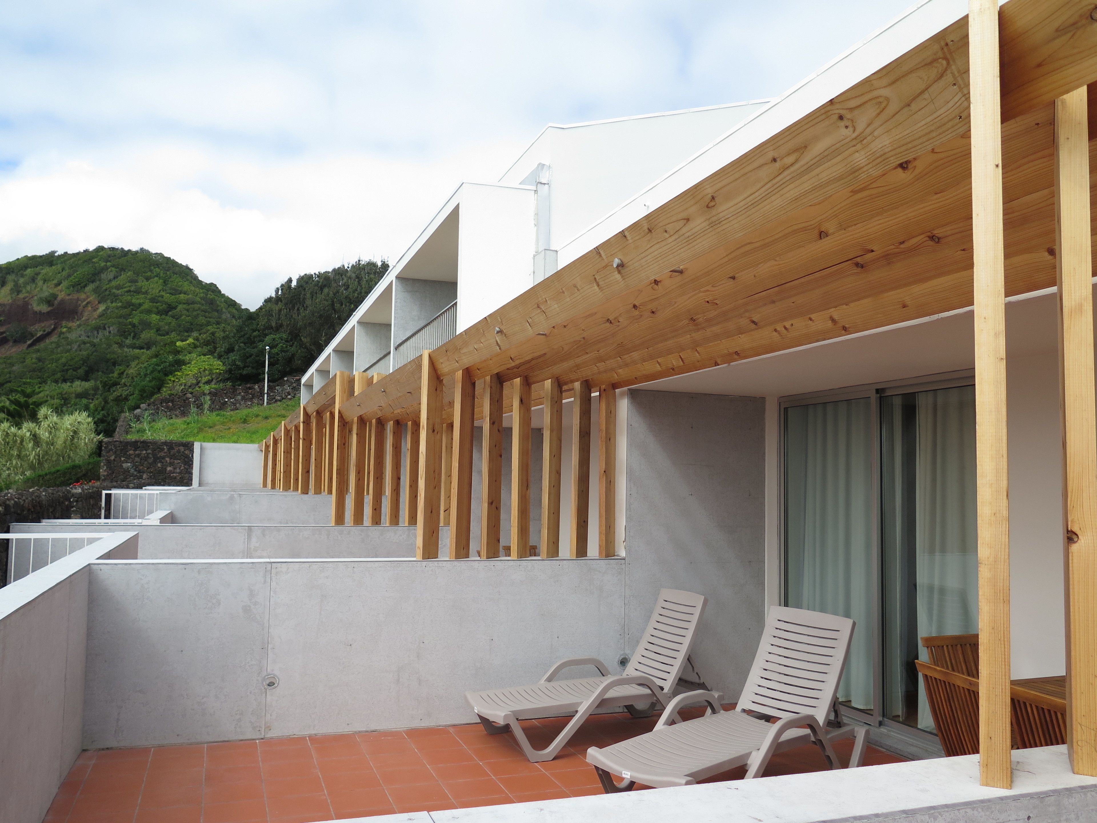 A balcony with wooden beams, a concrete floor, and two lounge chairs.