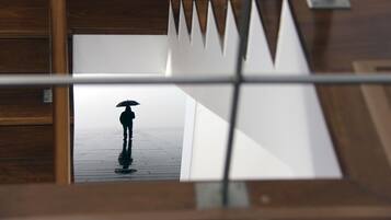 Uma pessoa segurando um guarda-chuva caminhando sobre um piso de madeira molhado.