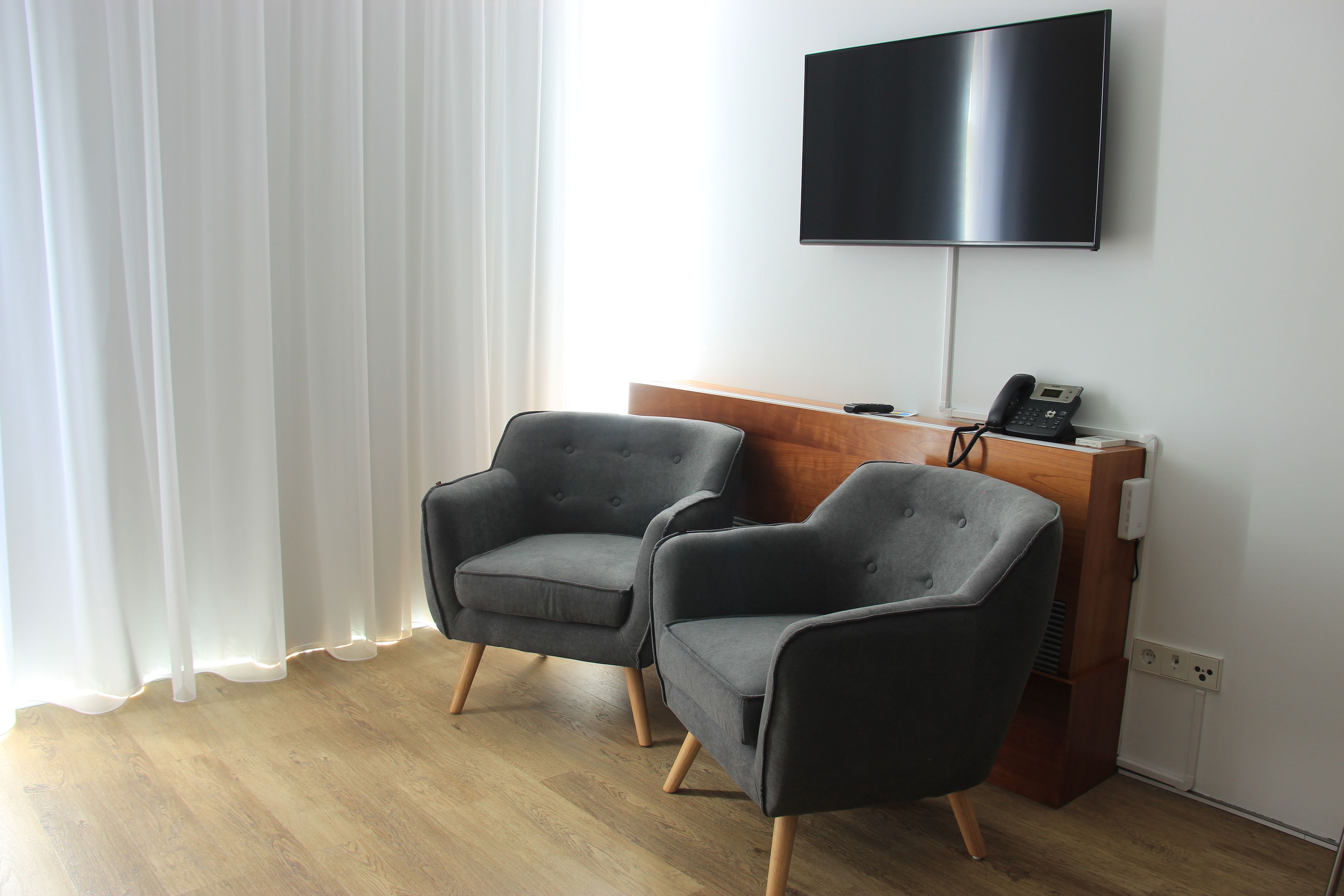 Een hotelkamer met twee grijze fauteuils, een houten bureau met een flatscreen televisie en een witte wand.
