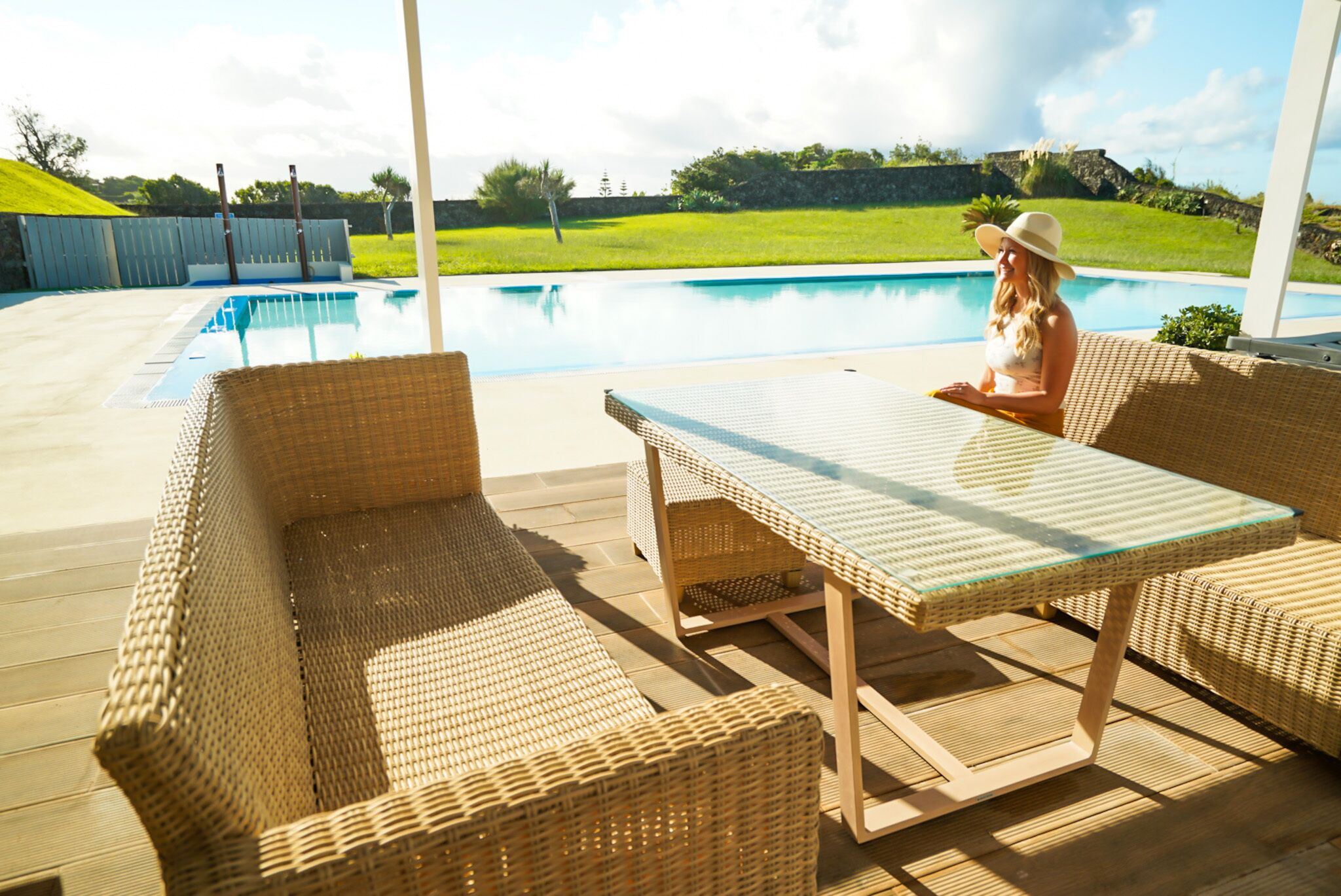 Zona de piscina con mobiliario de mimbre y una mesa de vidrio.