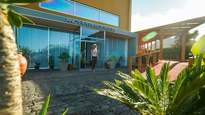 A building labeled "ANC EXPERIENCE RESORT" with a paved courtyard, potted plants, and a wooden pergola. - ANC Resort (Lagoa)