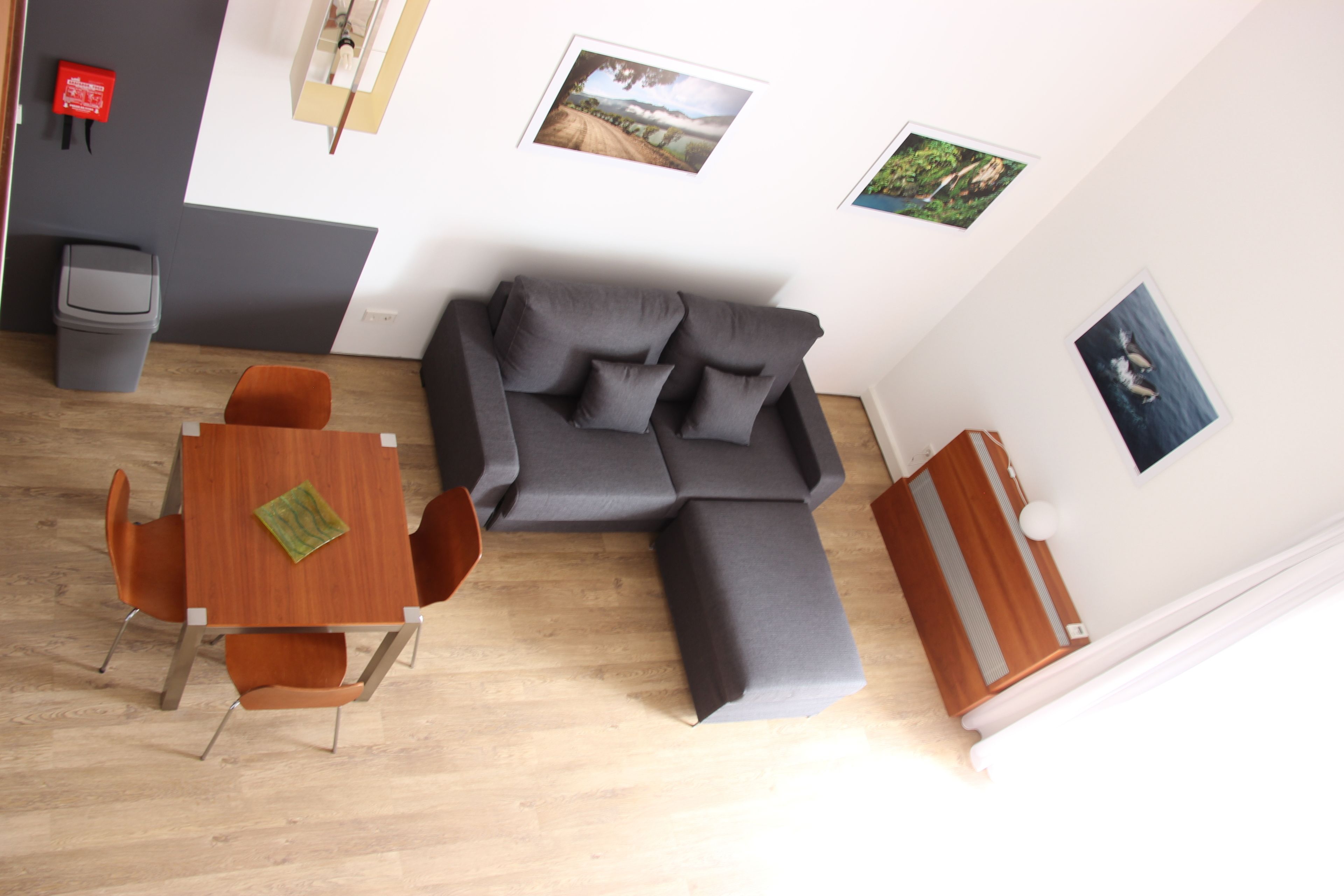 A modern living room with a grey sectional sofa, a wooden dining table with orange chairs, and a small wooden cabinet.