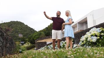 A couple standing in a garden with a view of a hillside and a building in the background.