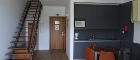 A modern kitchen with a microwave, sink, and orange chairs. There is a wooden staircase leading to an upper level.