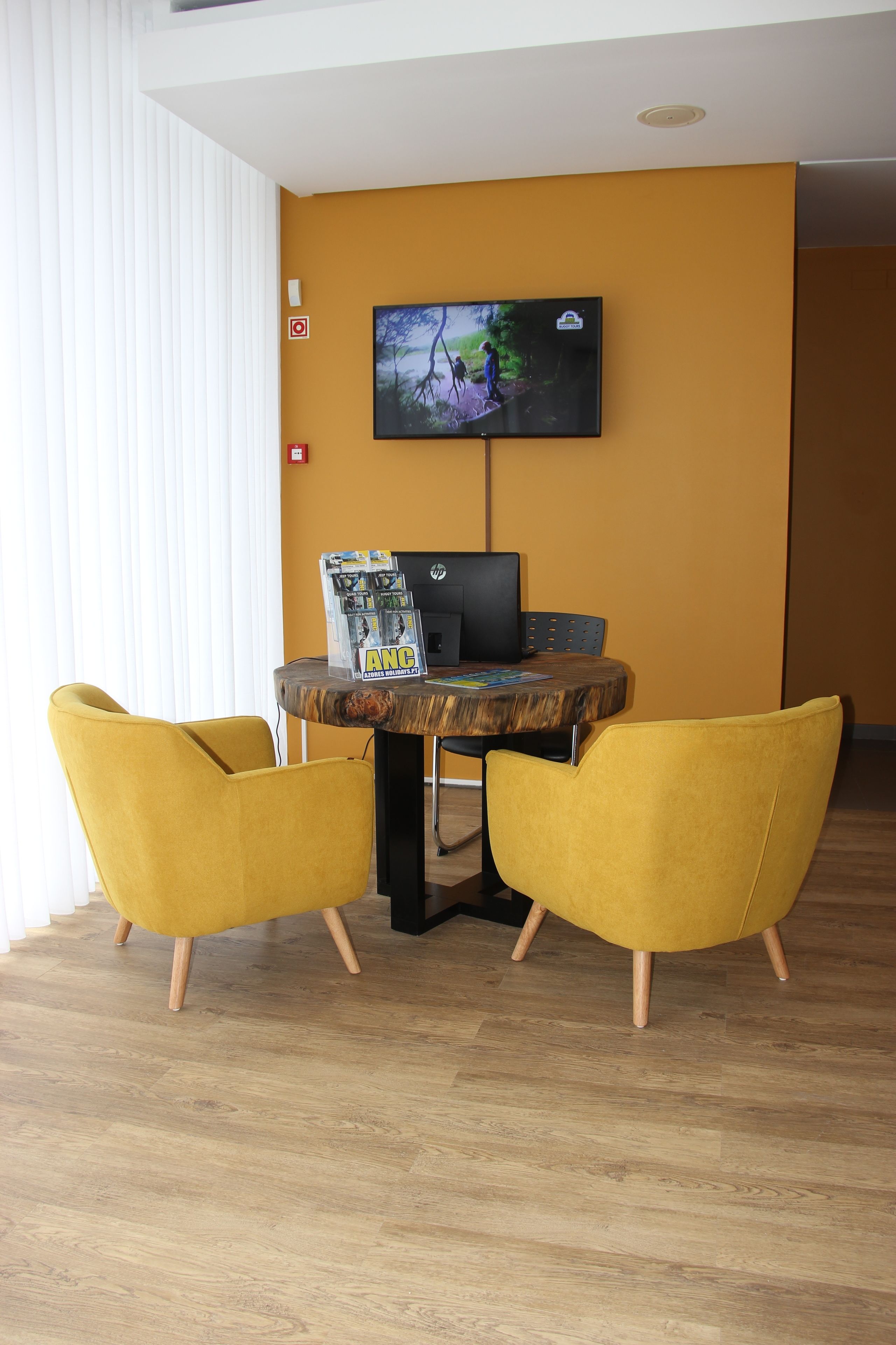 A room with a wooden table, two yellow chairs, a flat-screen TV on the wall, and a laptop on the table.