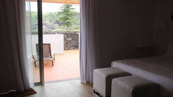 A bedroom with a large bed, a wooden floor, and a view of a patio with a chair and a stone wall.