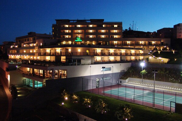 Un hotel de varios pisos con cancha de tenis y zona de estar al aire libre.