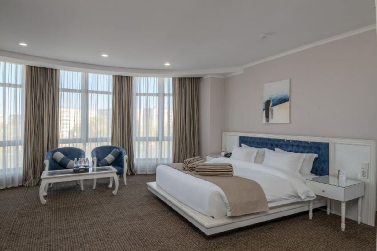 A hotel room with a large bed, two chairs, a small table, and a nightstand.