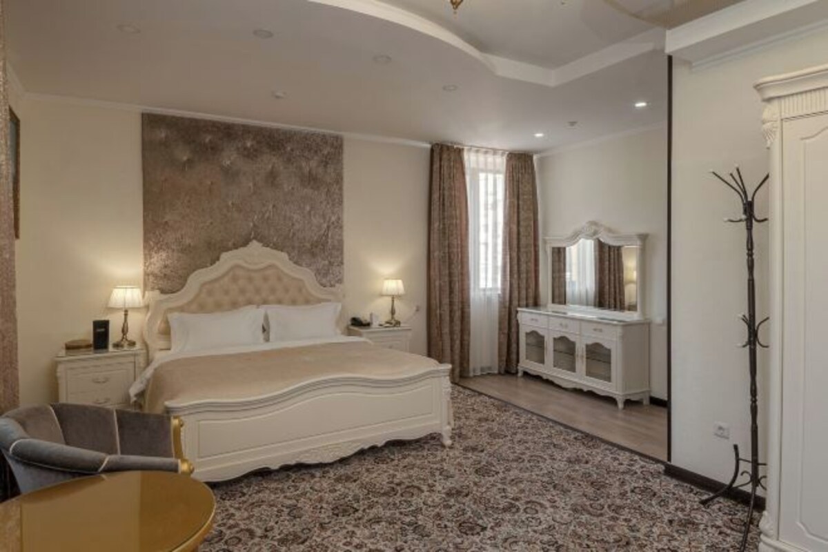 A bedroom with a large bed, a nightstand, a dresser, a mirror, and a chair.