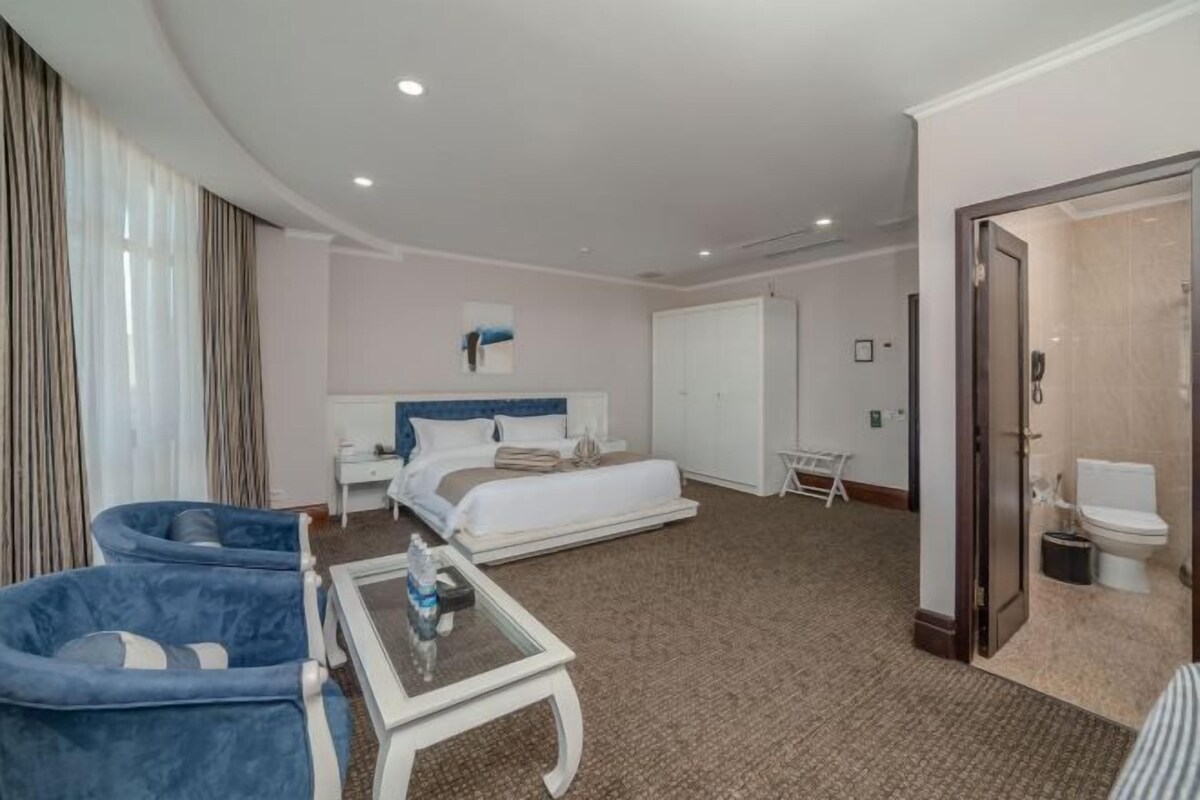 A hotel room with a bed, a desk, a chair, a small table, and a bathroom.