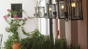 Una hilera de luces tipo farol negro en una pared, con una planta en maceta y una ventana que ofrece vista a un edificio al fondo.