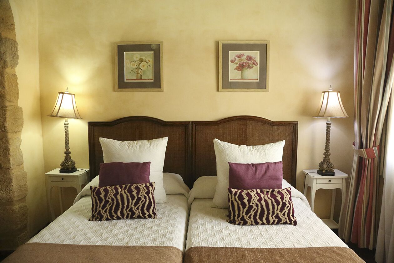 Una cama doble con dos almohadas, un cabecero de madera y dos mesitas de noche con lámparas.