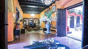 Una habitación con piso de madera, un candelabro, un jarrón grande con flores y un tapete de cuero de vaca.
