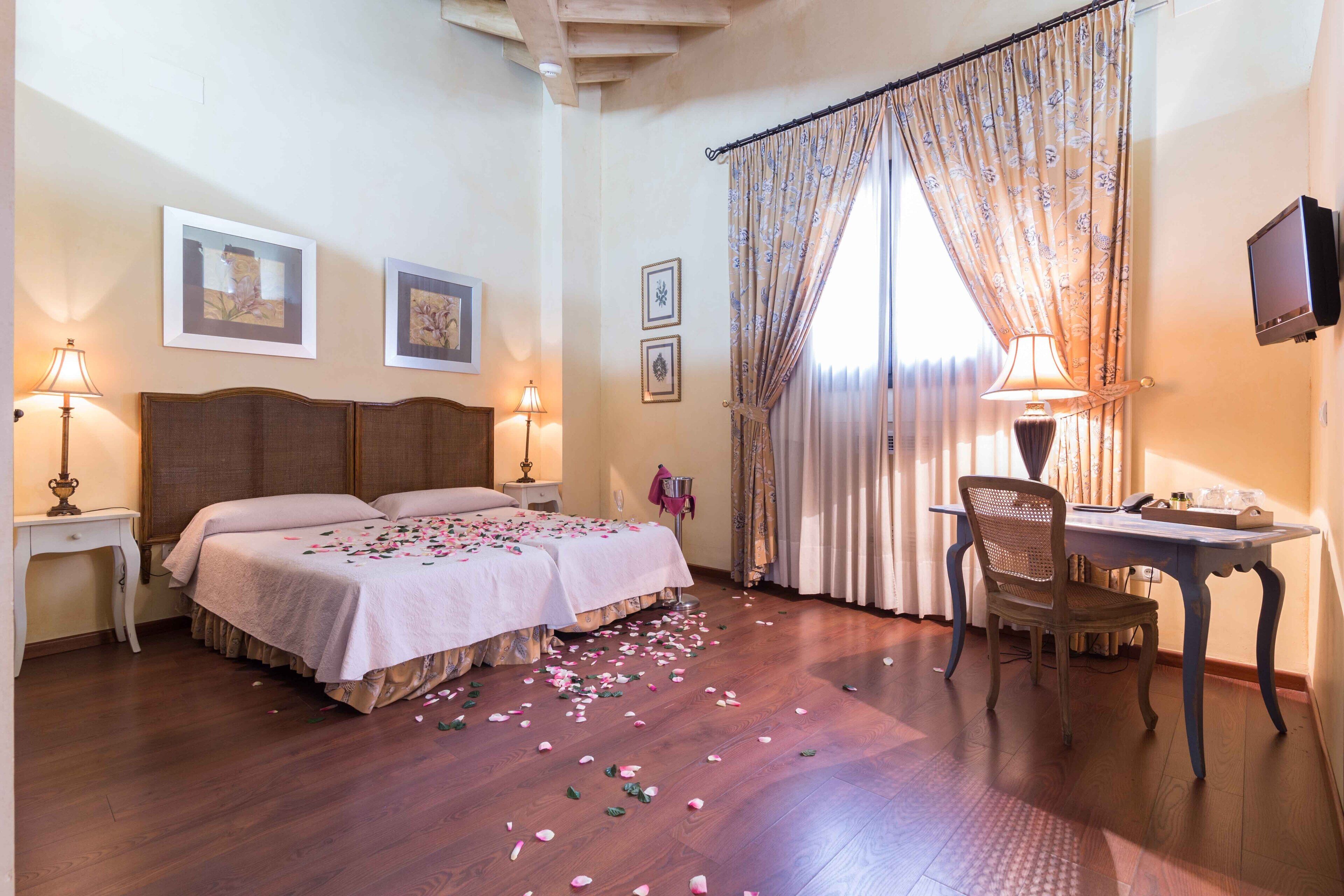 A hotel room with a double bed, a desk with a chair, a television, and a large window with curtains.