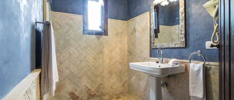 A bathroom with a herringbone tile wall, a pedestal sink, a mirror with a gold frame, and a handheld hair dryer.