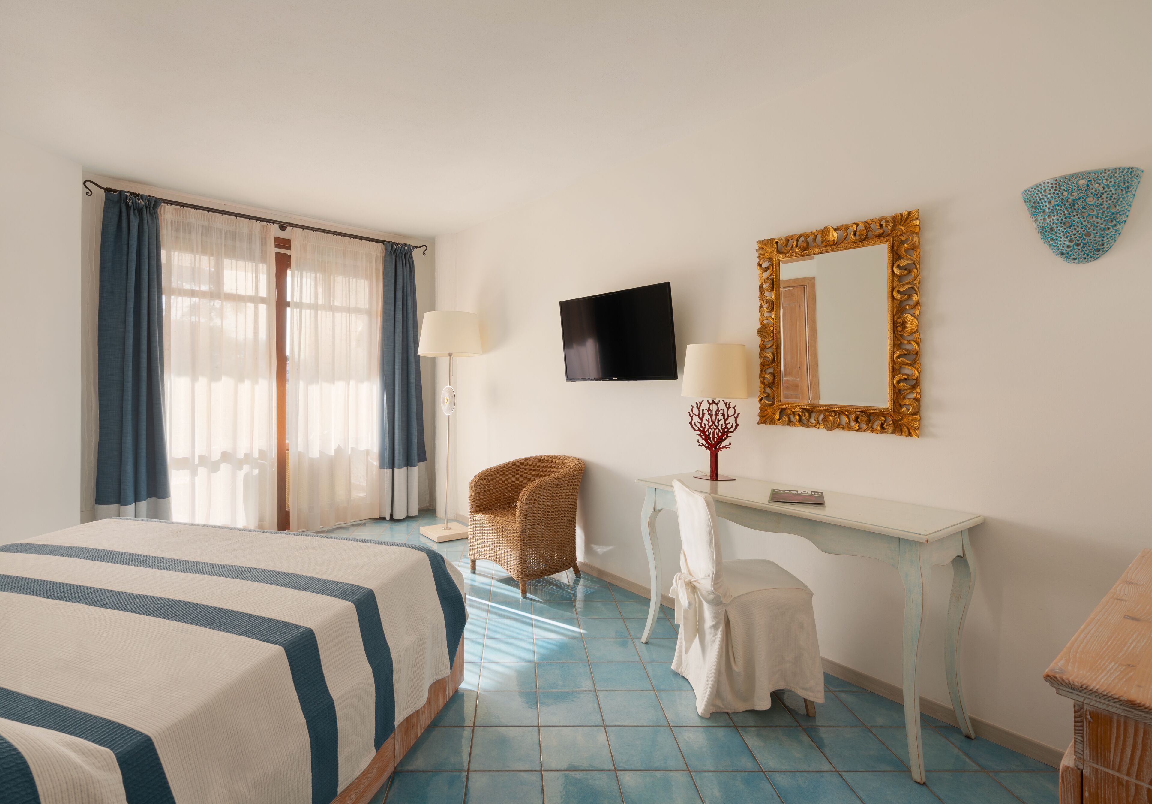 Quarto de hotel com uma cama, uma mesa, uma cadeira, uma televisão e um espelho.