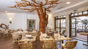 Un restaurant avec des meubles en bois, une grande sculpture d’arbre au plafond et de grandes fenêtres.